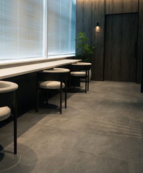 ブラインドのある大きな窓際に設置されたカウンター席とシンプルな椅子が並ぶ待合スペース